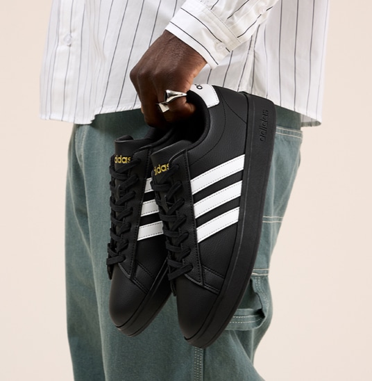 man holding black adidas shoes
