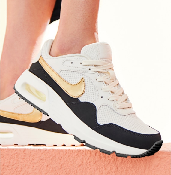feet of person wearing white black and gold nike airmax