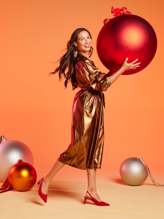 a woman holding a giant ornament wearing red dress heels