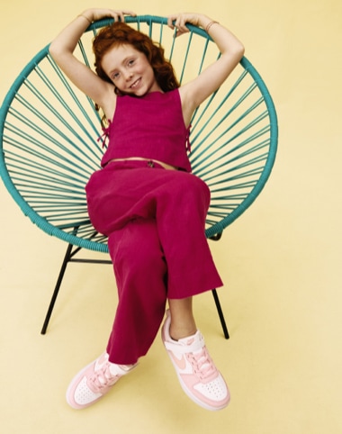 young girl sitting in outdoor chair wearing pink and white nike court sneakers