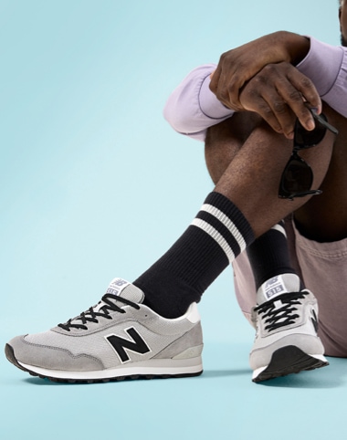 legs of person sitting down wearing black and grey new balance retro sneakers with black high top socks