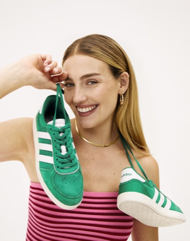 woman in red and pink striped shirt holding green adidas soccer inspired sneakers