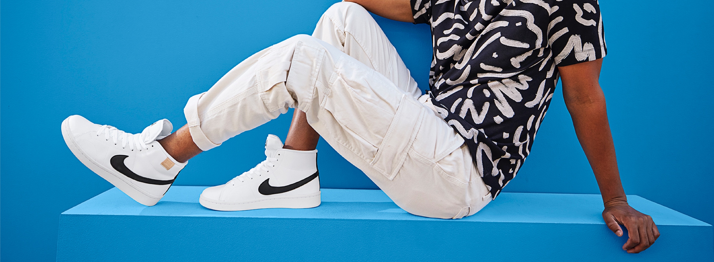 young man wearing white pants with white hight top nike sneakers and black swoosh