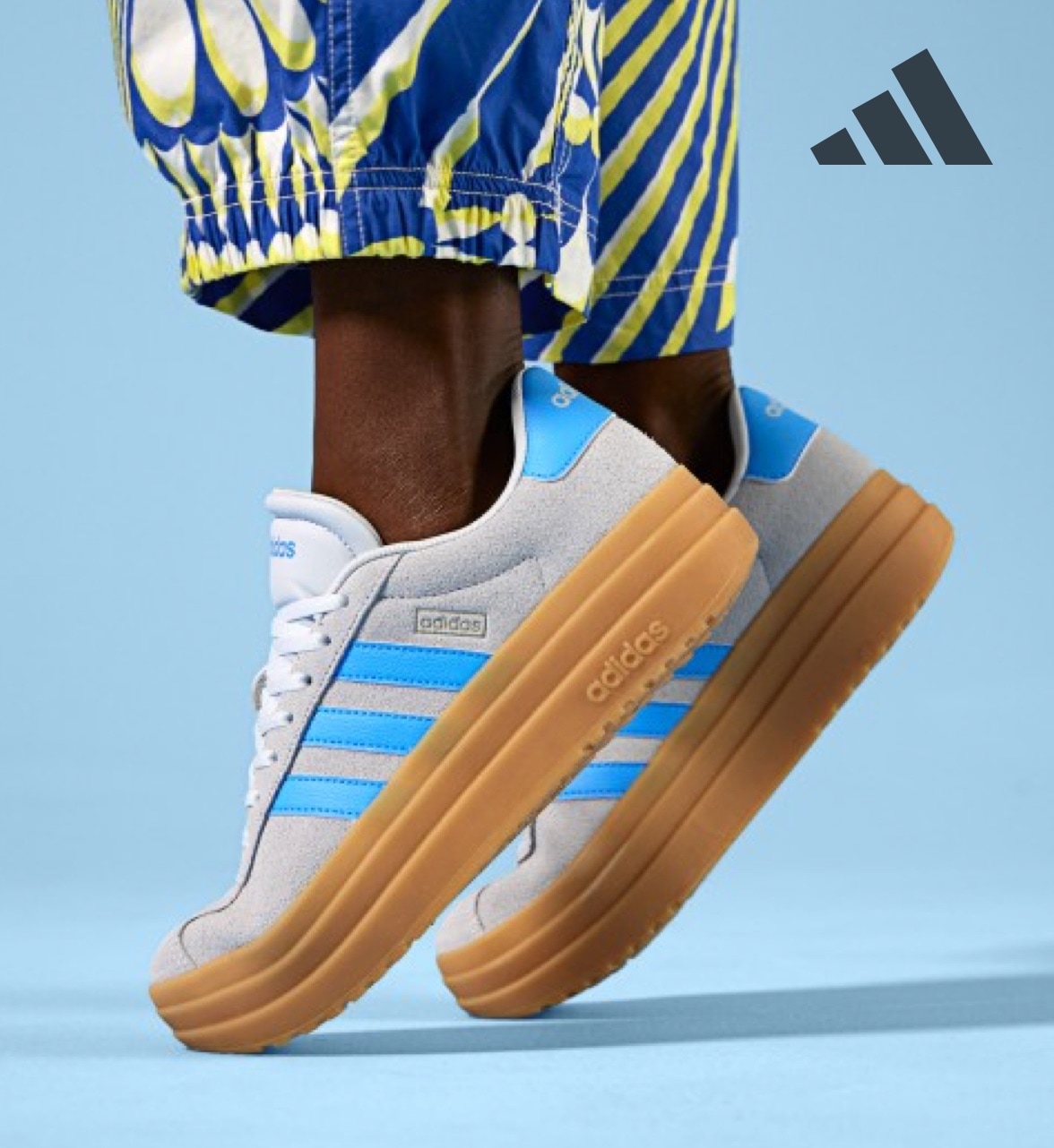 feet of person in blue and yellow printed pants wearing white and blue adidas court sneakers