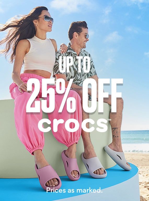 man and woman sitting on block on the beach wearing crocs slides on sale. up to 25% off crocs.