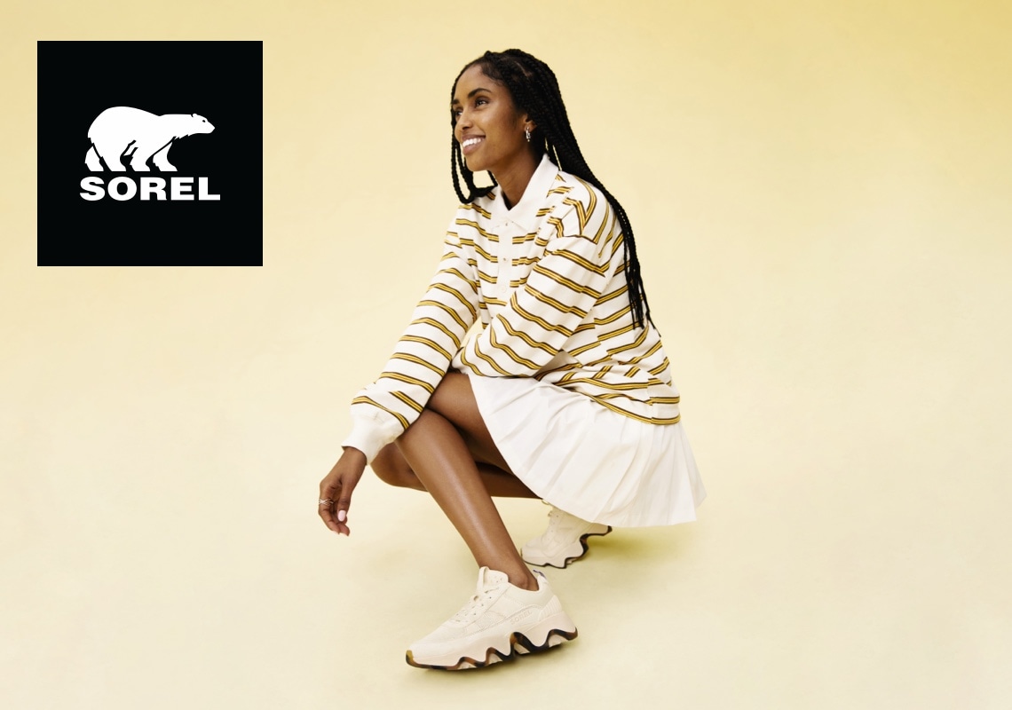 woman squatting down wearing sorel tennis shoes with sorel logo