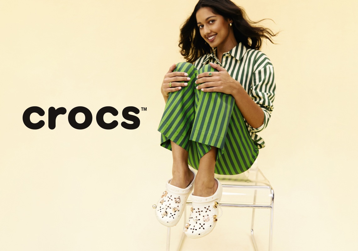 woman in striped set sitting on clear stool holding her legs up wearing crocs