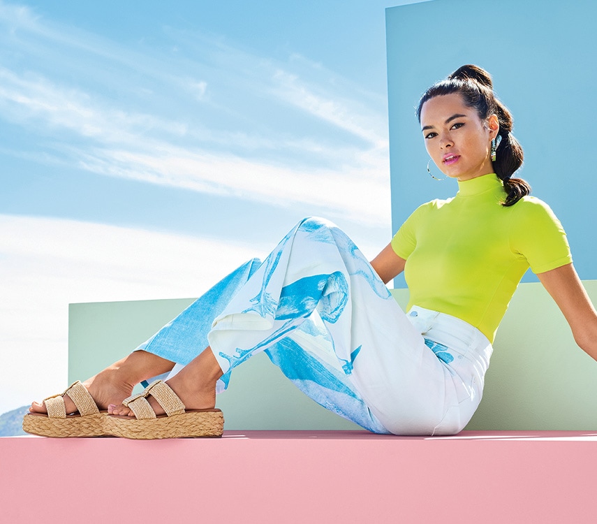 woman in blue pants and highlighter green top sitting wearing platform sandals
